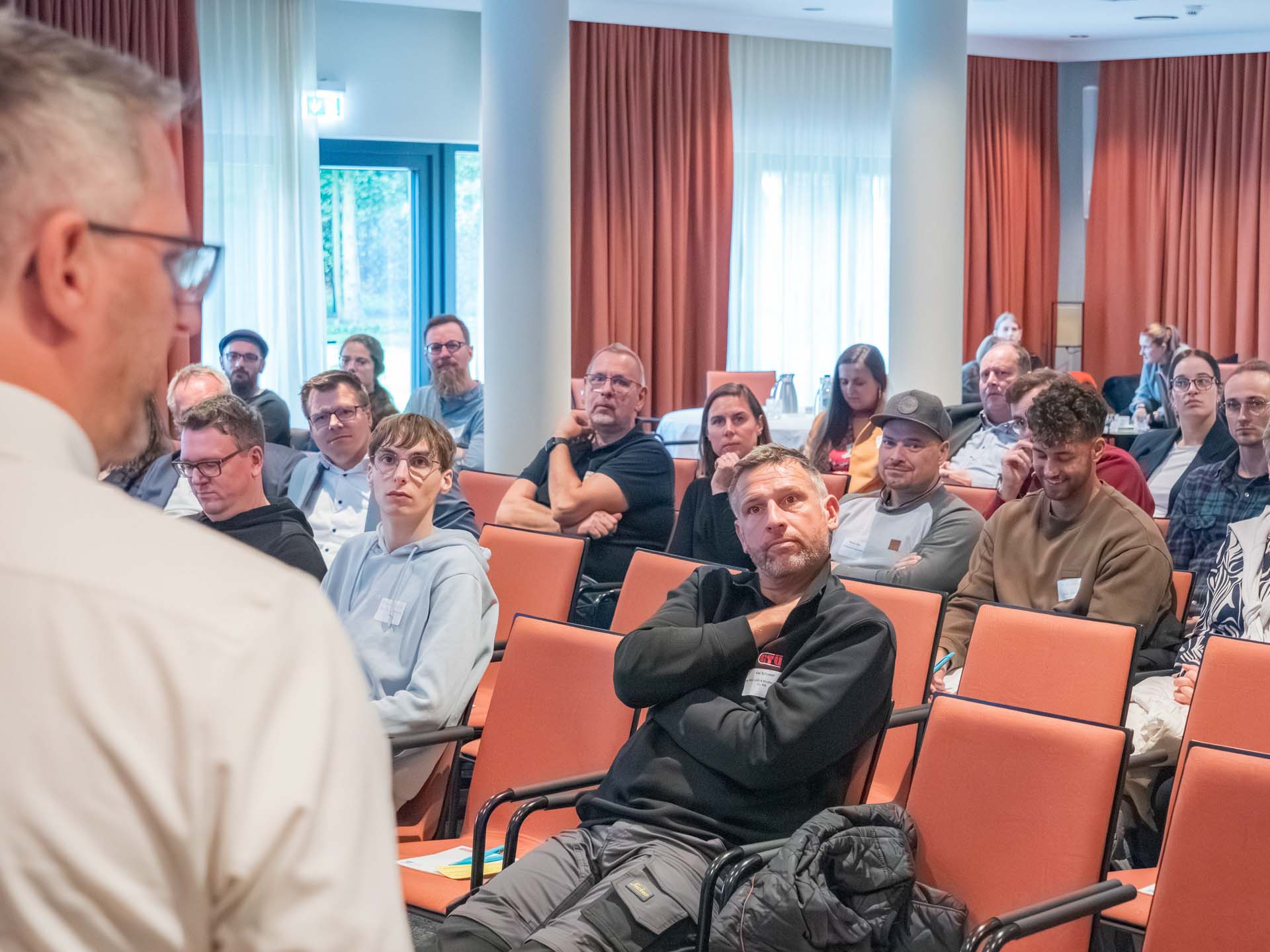 viele Personen sitzen in Stuhlreihen und schauen nach vorn zum Vortragenden
